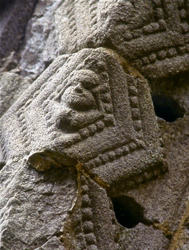 An Irish sheela-na-gig, carved into the front arch of the Nun's Chapel in Clonmacnoise. This is a closeup; the actual size of the sheela was probably only five inches in the diamond. You can see her face, and just make out her feet behind her head, with a display of her crotch below. ©Laurel Kallenbach