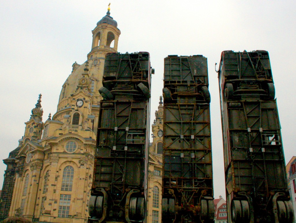 An art installation titled "Monument" recreates an image from the Syrian civil war: buses propped up vertically in an Aleppo street as a barricade against sniper fire. The artist is Syrian-German artist Manaf Halbouni. In the background is the Frauenkirche. Photo © Laurel Kallenbach