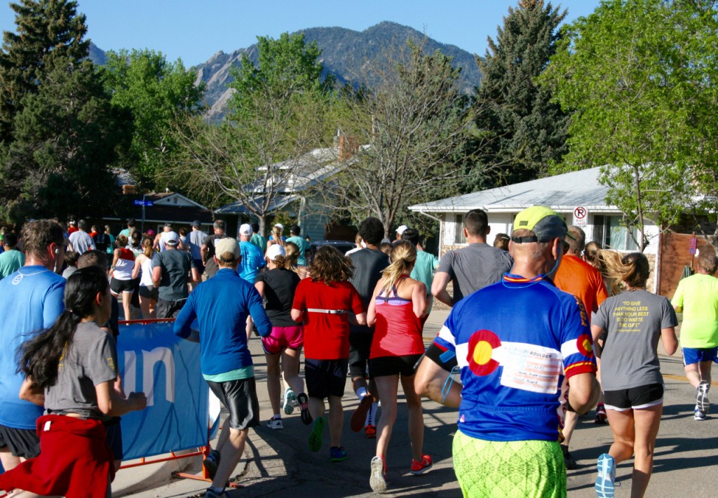 A guy with the Colorado state flag on his shirt runs by. The Flatirons and the mountains look on. ©Laurel Kallenbach